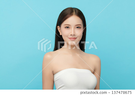 A beautiful young Asian woman with clean, fresh skin against a blue background. Skincare, facial treatment, cosmetology, beauty, and spa. An elegant portrait of an Asian woman. 137478675