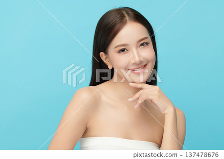 A beautiful young Asian woman with clean, fresh skin against a blue background. Skincare, facial treatment, cosmetology, beauty, and spa. An elegant portrait of an Asian woman. 137478676