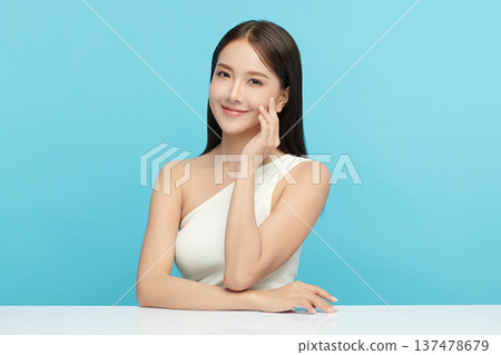 A beautiful young Asian woman with clean, fresh skin against a blue background. Skincare, facial treatment, cosmetology, beauty, and spa. An elegant portrait of an Asian woman. 137478679