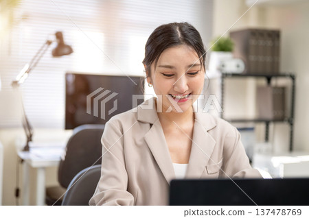 Pretty asian businesswoman or office worker looking down and typing on laptop while sitting at table Pretty asian businesswoman or office worker looking down and typing on laptop while sitting at table 137478769