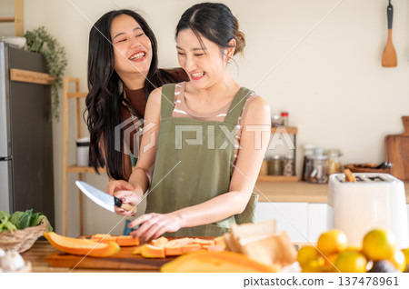 Asian woman looking at girlfriend holding knife cutting papaya on board at kitchen cooking counter. 137478961