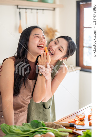 Happy asian woman feeding a girlfriend as standing at kitchen cooking counter with food ingredients. 137478966