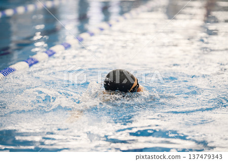 Photo of a man wearing special hat for swimming. Man swimming breaststroke in swimming pool. Professionale male swimmer training. 137479343