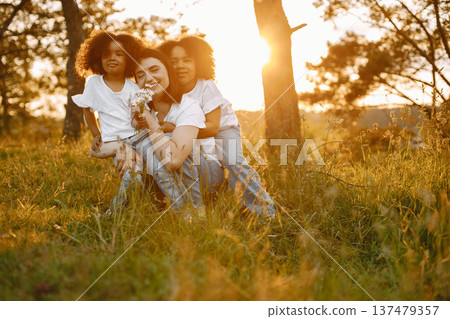Photo of caucasian mother and two her african american daughters embracing together outdoors. Girls has black curly hair. Mother and daughers wearing white t-shirts. Photo of caucasian mother and two her african american daughters embracing together outdoors. Girls has black curly hair. Mother and daughers wearing white t-shirts. 137479357