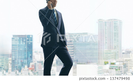 A male business person talking on a smartphone with a city in the background A male business person talking on a smartphone with a city in the background 137479498