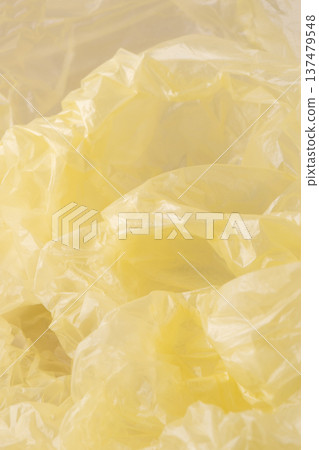 Crumpled yellow plastic creating an abstract background texture. Showing wrinkles, folds, and highlights on transparent polyethylene material Crumpled yellow plastic creating an abstract background texture. Showing wrinkles, folds, and highlights on transparent polyethylene material 137479548