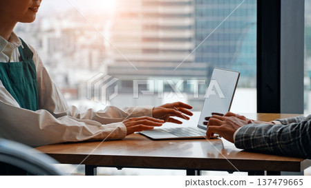 A shop assistant and a business person having a meeting while looking at a laptop A shop assistant and a business person having a meeting while looking at a laptop 137479665