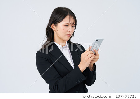 一位女商人神情憂慮地看著她的智慧型手機螢幕。 137479723