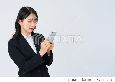 A businesswoman looking at her smartphone screen with a troubled expression A businesswoman looking at her smartphone screen with a troubled expression 137479725