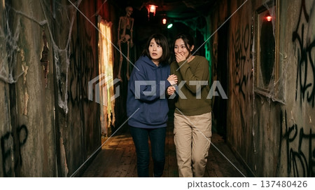 Two women walking fearfully through a haunted house at an amusement park 137480426