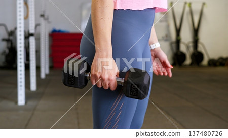 Woman training in gym holding dumbbell for fitness workout Woman training in gym holding dumbbell for fitness workout 137480726