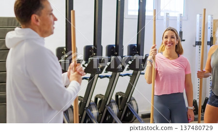 Fitness trainer leading women in gym exercise with poles 137480729