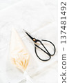 A piping bag and scissors placed together on parchment paper, highlighting tools used in creating intricate royal icing cookie designs. 137481492
