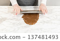 Front-facing view of hands using a rolling pin to flatten spiced gingerbread cookie dough on a marble countertop, demonstrating the preparation process. 137481493