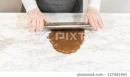 Front-facing view of hands using a rolling pin to flatten spiced gingerbread cookie dough on a marble countertop, demonstrating the preparation process. Front-facing view of hands using a rolling pin to flatten spiced gingerbread cookie dough on a marble countertop, demonstrating the preparation process. 137481493