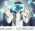 A young girl wearing a virtual reality headset, interacting with a digital environment. Her hands are raised as if engaging with virtual objects, while futuristic graphics surround her, creating an 137481545