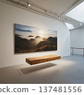 A clean gallery space displays a framed mountain landscape artwork on a white wall. Minimal seating and lighting focus attention on the art. The mood feels quiet and refined. 137481556