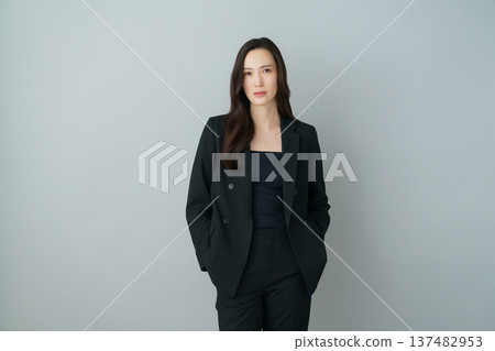 灰色背景上的年輕日本女性身穿黑色西裝的時尚肖像 137482953