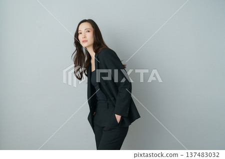 Fashion portrait of a young Japanese woman in a black suit on a gray background 137483032