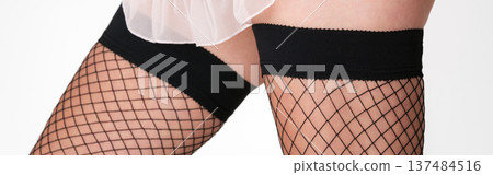 Close-up of woman's legs wearing alluring black fishnet stockings with wide black elastic tops. Close-up of woman's legs wearing alluring black fishnet stockings with wide black elastic tops. 137484516