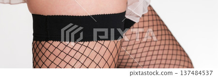 Close-up shot of a woman's legs adorned with black fishnet stockings, featuring a detailed net pattern opaque top band. Close-up shot of a woman's legs adorned with black fishnet stockings, featuring a detailed net pattern opaque top band. 137484537