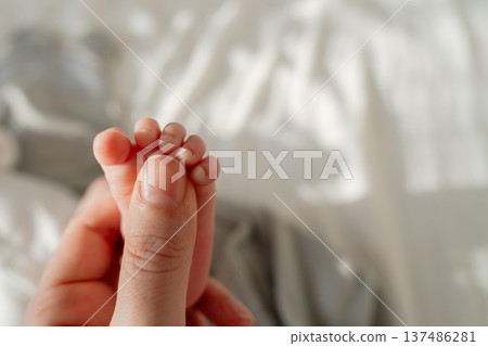 Close up of tiny newborn toes gently held by parent. Soft natural light and blurred background create intimate and heartwarming family moment. 137486281