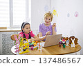 A mother and daughter wearing bunny ears are watching an online tutorial on a laptop to learn how to decorate Easter eggs together 137486567