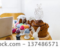 A festive table setting features traditional Easter cakes, colorful painted eggs in holders, and a 'Happy Easter' cake topper with bunny ears 137486571