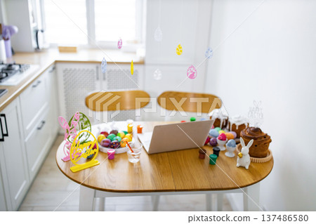 A kitchen table is set up for Easter egg decorating with painted eggs, cakes, and a laptop for virtual celebration A kitchen table is set up for Easter egg decorating with painted eggs, cakes, and a laptop for virtual celebration 137486580