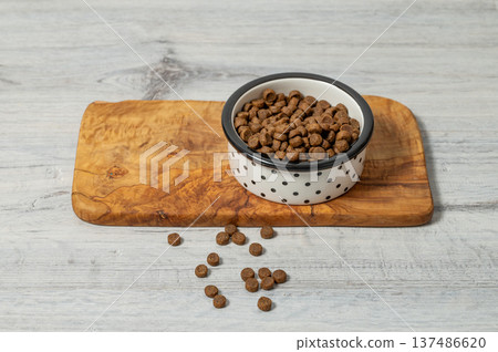 A bowl of dry dog or cat food on a wooden board on a gray wooden floor. 137486620