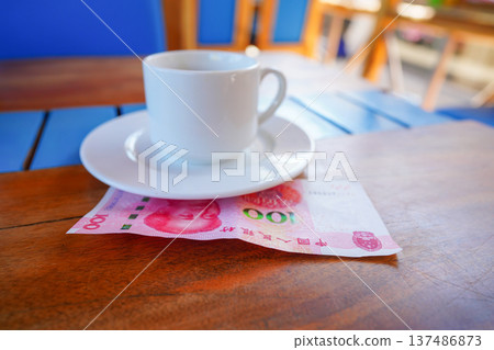 Coffee cup on table with hundred yuan bill in cafe. Payment coffee drink on breakfast. Coffee cup on table with hundred yuan bill in cafe. Payment coffee drink on breakfast. 137486873