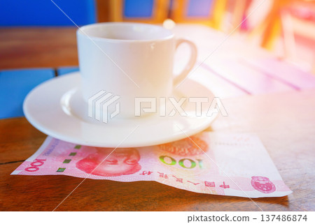 Coffee cup on table with hundred yuan bill in cafe. Payment coffee drink on breakfast. Coffee cup on table with hundred yuan bill in cafe. Payment coffee drink on breakfast. 137486874