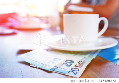 Coffee cup on table with Euro money bill in cafe. Payment coffee drink on breakfast. EC Bill money Coffee cup on table with Euro money bill in cafe. Payment coffee drink on breakfast. EC Bill money 137486878