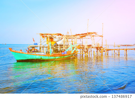 Fishing boat at wooden pier on clear blue sky, calm ocean water in daytime in coastal. Fishing boat at wooden pier on clear blue sky, calm ocean water in daytime in coastal. 137486917