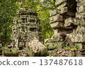 Ancient stone temple tower covered in green moss and surrounded by lush forest trees at abandoned archaeological site in Siem Reap 137487618