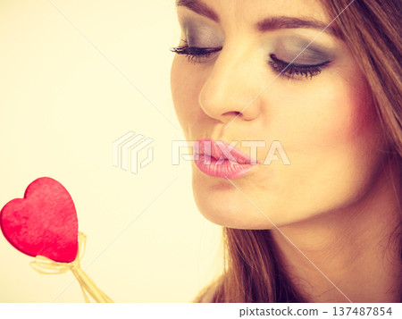 Flirty woman holding red wooden heart on stick Flirty woman holding red wooden heart on stick 137487854