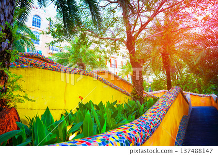 Vibrant stairs walkway among trees, colorful walls in tropical sunset. Winding path leads greenery 137488147