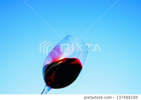 Red wine swirling on blue sky. Sommelier swirls with glass of red wine at sunset sky. Red Wine  137488189