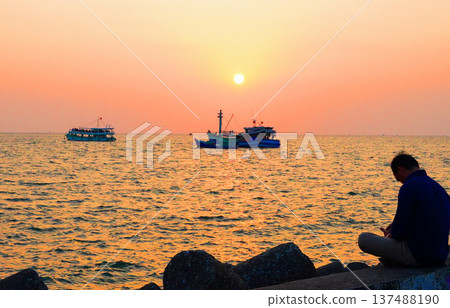 Sunset at shore with fishing boats. Person sitting on pier by sunset sea. Sunset over ocean Sunset at shore with fishing boats. Person sitting on pier by sunset sea. Sunset over ocean 137488190