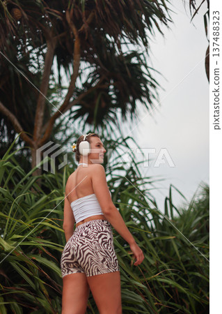 Woman In Summer Resort Attire. Relaxed Summer Style Showcased Amidst Vibrant Green Palm Leaves Woman In Summer Resort Attire. Relaxed Summer Style Showcased Amidst Vibrant Green Palm Leaves 137488323