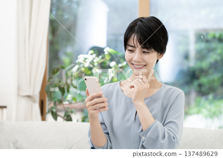 坐在沙發上使用智能手機的年輕女性 坐在沙發上使用智能手機的年輕女性 137489629