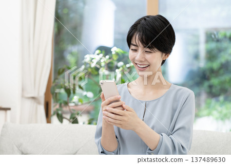坐在沙發上使用智能手機的年輕女性 坐在沙發上使用智能手機的年輕女性 137489630