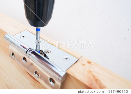 Screwdriver is used to attach hinge to wooden door frame. Screwdriver is used to attach hinge to wooden door frame. 137490330
