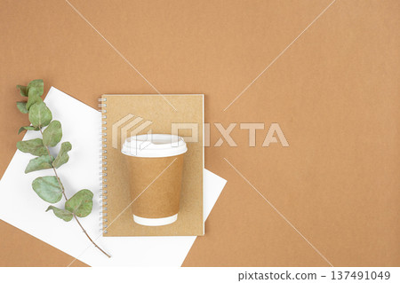 Craft paper coffee cup, notebook and eucalyptus sprig on eco background, flat lay. 137491049