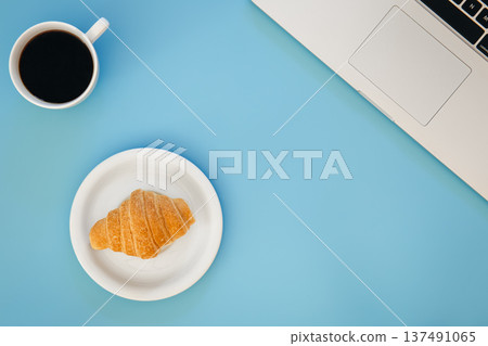 Croissant, cup of coffee and laptop on a blue background, flat lay. Croissant, cup of coffee and laptop on a blue background, flat lay. 137491065
