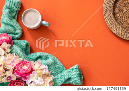 Cup of coffee, flowers and knitted element on orange background, flat lay. 137491169