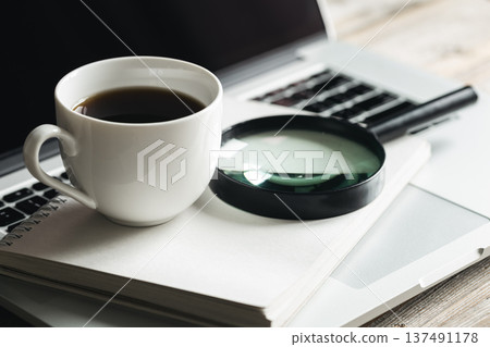 Cup of coffee, magnifier, notepad and laptop at workplace, close-up. Cup of coffee, magnifier, notepad and laptop at workplace, close-up. 137491178