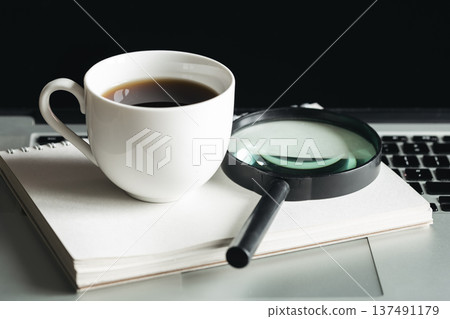 Cup of coffee, magnifier, notepad and laptop at workplace, close-up. 137491179