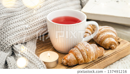 A cup of red tea, a candle, a croissant and a knitted element on a tray in bed. 137491216