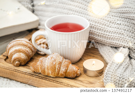 A cup of red tea, a candle, a croissant and a knitted element on a tray in bed. A cup of red tea, a candle, a croissant and a knitted element on a tray in bed. 137491217